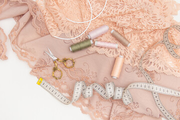 Peach lace, scissors, threads, measuring tape and bra bones. Top view. Materials for sewing lingerie
