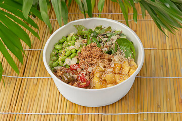 Bowl of chicken poké with rice , mango, pineapple , almonds, soy and teriyaki, isolated on bamboo table