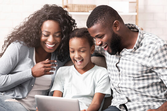 Cheerful african american family of three watching funny videos on digital tablet at home.
