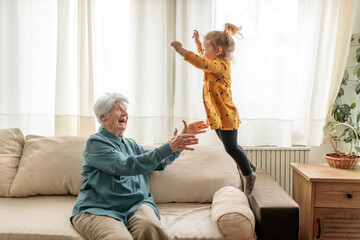 Toddler girl jumping on the sofa, playing with her great grandmother