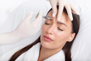 Young woman recieving injection of anti-aging botox filler to forehead from professional...