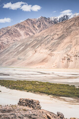 Pyanj River flows in Wakhan Valley among rocky high mountains against snow-capped peaks and glaciers in Tajikistan's Tien Shan mountains, landscape for background
