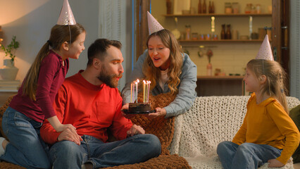 Happy birthday event Caucasian family mom children congratulate dad surprise birth party cheerful parents little girls kids daughters siblings festive caps celebrate blowing candles cake together home