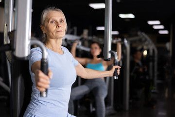 Older sportswoman training at chest fly machine in gym