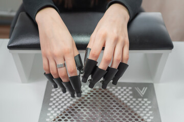 Process removing gel polish from nails in a beauty salon close up. Woman hands with set of plastic caps tool with acetone for remove shellac. Concept nails and hands care 
