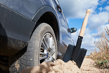 A car stuck in the sand with a shovel placed nearby, ready for use. The image captures a close-up...
