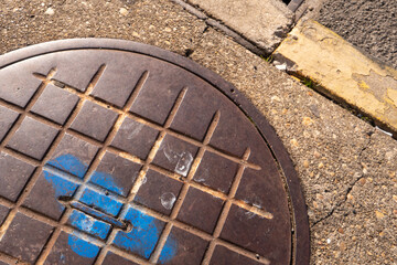 heavy steel man hole cover installed in the street, showing signs of wear from foot traffic and weathering over decades