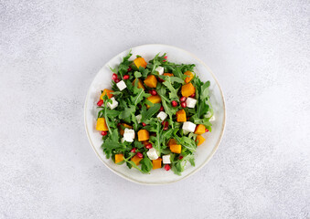 Pumpkin salad with arugula, feta cheese and pomegranate seeds on a gray background. Top view. Thanksgiving Dishes.