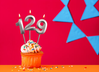 Birthday cupcake with candle number 129 on a red background with blue pennants