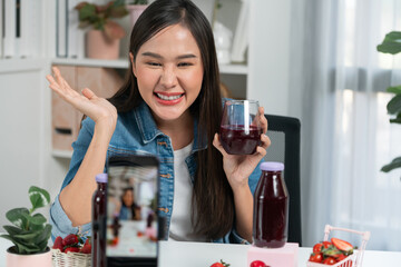Smiling young beautiful Asian reviewing tasty mixed strawberry and cherry juice detox drinks, showing healthy product to promote for special promotion selling on social media online record. Stratagem.