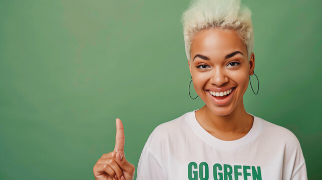 A vibrant young woman with short, dyed blonde hair and a bright smile points upward while wearing a "Go Green" t-shirt, set against a green background, promoting environmental awareness and sustainabi