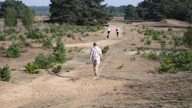 middle-aged woman walks through the Sahara-Lommel National Park towards some unrecognizable people walking their dog, then into the distance, into an out-of-focus area