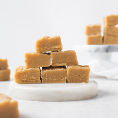 peanut butter fudge on a marble tray, soft peanut fudge squares stacked on a white tray