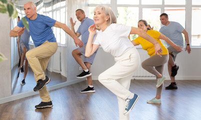 Expressive cheerful woman participating in upbeat Zumba class for group of seniors in mirrored...