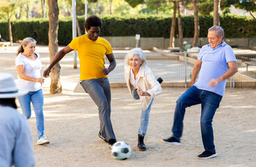 Obraz premium Group of cheerful mixed-race men and women of different age having fun while playing football in city park at sunny day