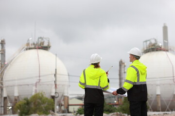 Male & Female engineers stand Discussing the building plan at the site, Engineers working outdoors and use walkie-talkies against the Round gas storage tank in the background