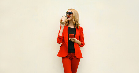 Stylish businesswoman drinking coffee, beautiful woman using smartphone in red business suit