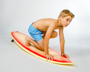 Young shirtless preteen surfer boy preparing to stand up on surfboard in studio with white...
