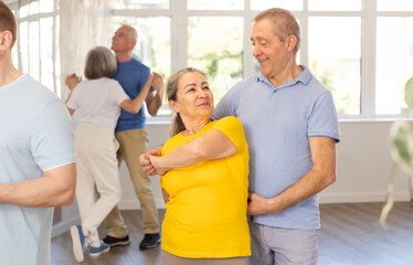 Fototapeta premium Smiling elderly woman with male partner in latin dance class. Social dancing concept