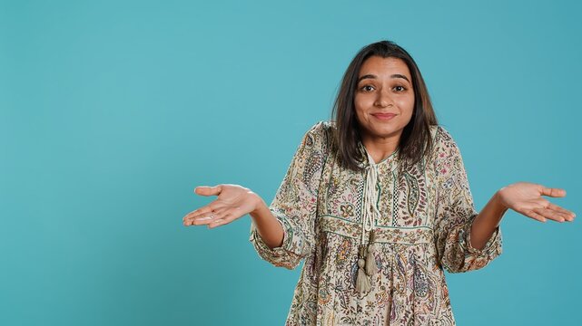 Indian woman shrugging shoulders, unable to provide answer, having detached apathy facial expression. Apathetic person doing hand gesturing showing lack of knowledge, studio background, camera A