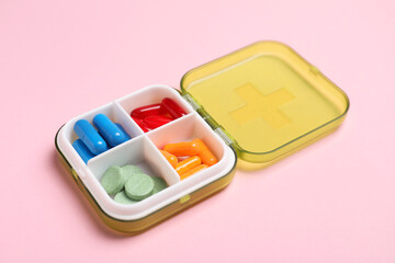 Different pills in organizer on pink background, closeup