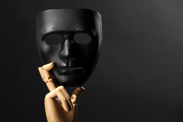 Wooden mannequin hand holding plastic mask on black background, space for text. Theatrical...