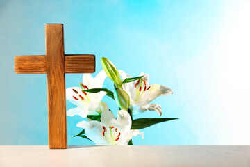 Wooden cross and beautiful lily flowers on table against light blue background, space for text....