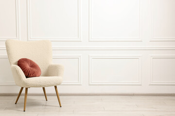 Soft armchair with pillow in light room. Space for text