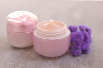 Jars of creams and ageratum flowers on gray table, closeup