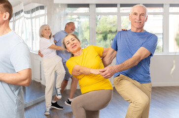Obraz premium Group of elderly men and woman in sportswear learning to dance latin salsa dance in dance class