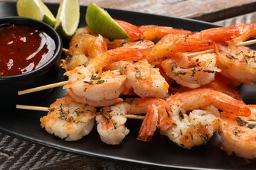 Delicious grilled shrimp skewers served with sauce and lime on wooden table, closeup