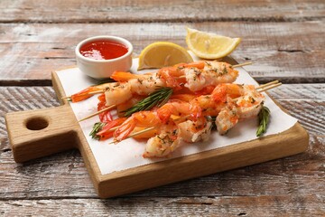 Delicious grilled shrimp skewers served with sauce and lemon on wooden table