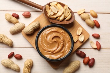 Tasty peanut butter in bowl and nuts on wooden table, flat lay
