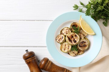 Tasty grilled zucchini slices with lemon and parsley on white wooden table, flat lay. Space for text