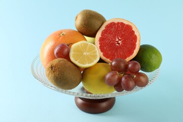 Glass vase with different fresh fruits on light blue background, closeup