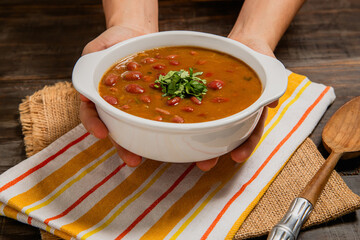 hands holding cranberry traditional colombian soup with cilantro topping