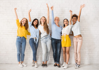 Obraz premium Hello. Diverse Women Waving Hands Smiling At Camera Standing Against White Brick Wall Indoor. Full Length