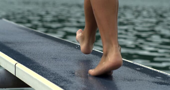 Slow-motion at 800 fps of a person walking on a diving board towards water, showing the wet feet and tension before the jump