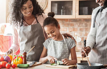 Kids at kitchen. Pretty little black girl cutting cucumber, helping parents with dinner, making healthy food, cropped, empty space