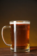 Mug with fresh beer on wooden table against dark background