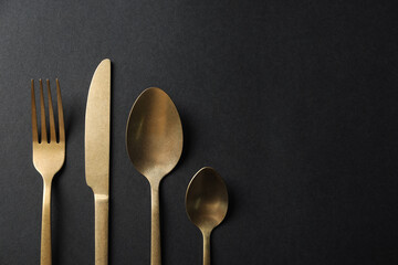 Elegant golden cutlery on black background, flat lay. Space for text