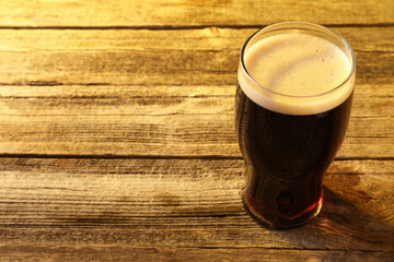 Glass of beer with froth on wooden table, space for text