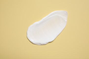 Face cream on pale yellow background, top view