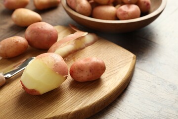 Fresh raw potatoes, peels and peeler on wooden table