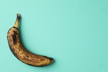 Overripe banana with dark spots on turquoise background, top view. Space for text