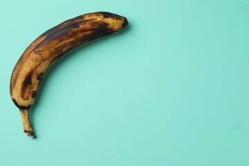 Overripe banana with dark spots on turquoise background, top view. Space for text