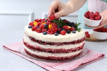 Woman decorating tasty sponge cake with berries at light grey table, closeup