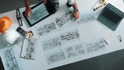 Top down view of engineer looking at tablet while using laptop to analysis building structure. Aerial view of architect checking at interior design at meeting table with project plan. Alimentation.