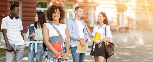 Happy beautiful afro student girl with backpack holding folder and workbook at university and...