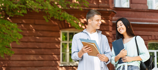 Cheerful couple of university friends resting between classes outdoors, chatting and smiling